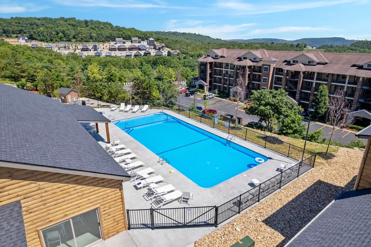 An inviting exterior shot of the swimming pool area, surrounded by lush greenery and residential buildings. The pool area is spacious, offering plenty of room for swimming, sunbathing, and hosting group gatherings, with the water reflecting the relaxed, leisurely mood of resort life.