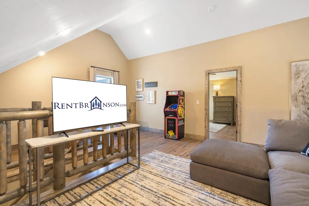 An inviting loft game area features a cozy sectional couch, a large TV, and a classic arcade game machine. Large windows let in natural light, creating a playful and relaxed atmosphere perfect for family game nights and multi-generational bonding.