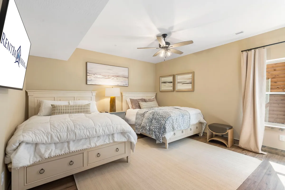 A spacious bedroom with two beds, decorative wall art, a table lamp, and a window dressed with curtains. The beds are neatly made and the room exudes a cozy, relaxing vibe, ideal for families or groups.