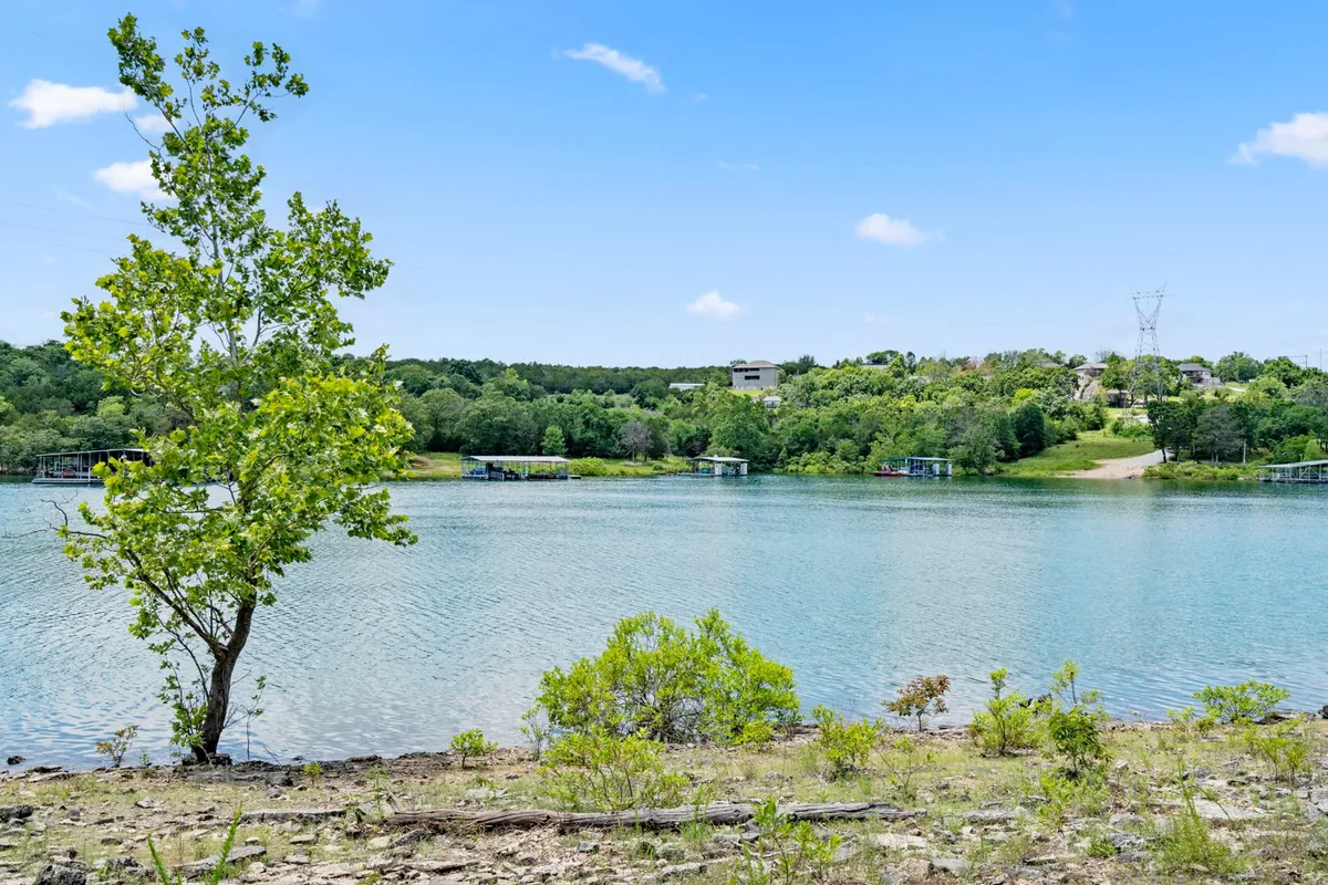 A serene view of Table Rock Lake at sunset, with the still water, distant shoreline, a prominent tree, and a wide-open sky. The peaceful setting invites early morning coffee or evening drinks while soaking in lakeside tranquility.