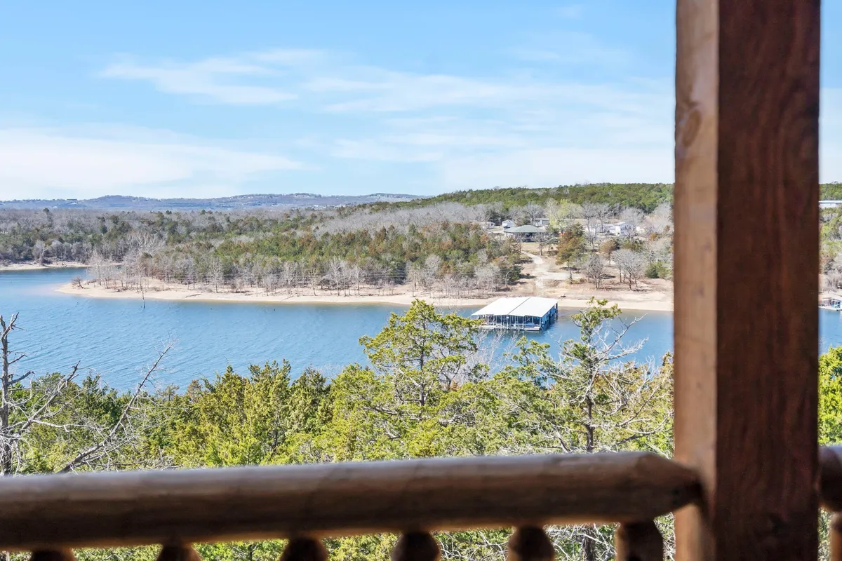A sweeping view overlooking a tranquil lake, framed by trees and a distant boathouse. The scene is peaceful and open, offering an inviting perspective for watching sunsets or simply soaking in the natural Ozark scenery.