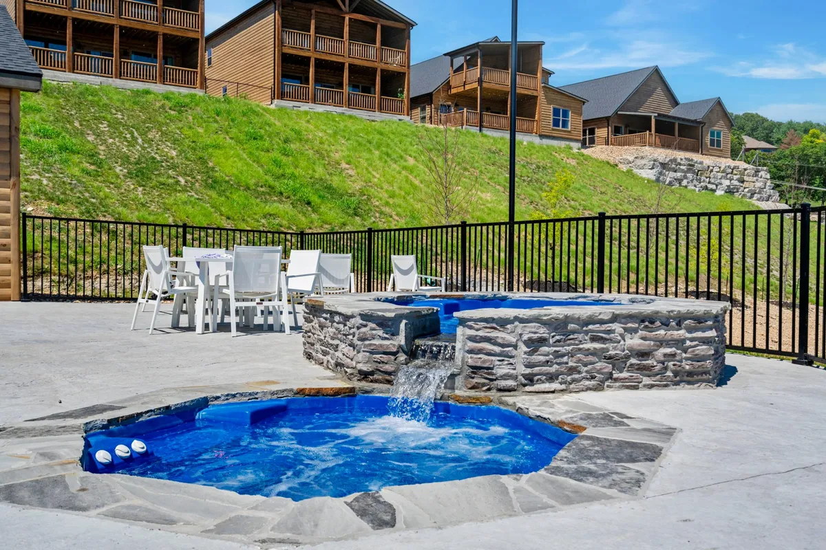 The image shows multiple hot tubs set on a spacious outdoor deck, with a dining table nearby and several cabins in the background. The setting exudes a sense of privacy and relaxation while providing space for socializing and enjoying the fresh air.